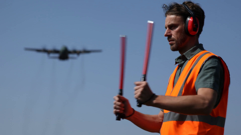 airport-worker-man-standing-show-position-leading-sign-airplane-flying-overhead_sfwdvyovx_thumbnail-full10-768x432